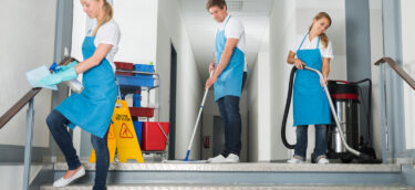 Group Of Happy Male And Female Janitor Cleaning Corridor With Cleaning Equipments